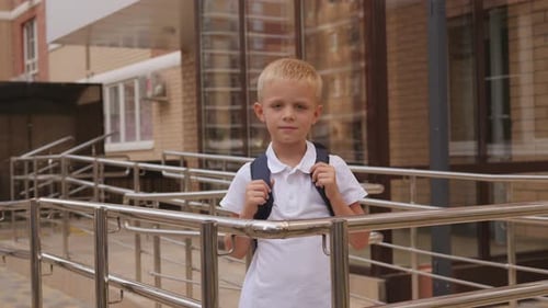 Portrait of a Small Schoolboy in a School Uniform with a Backpack Near a School