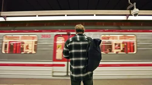 Brünetter Mann mit Rucksack steht in der U-Bahn und wartet