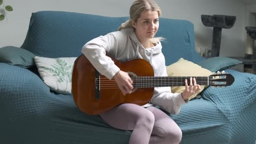 Young Woman Playing Acoustic Guitar on Sofa