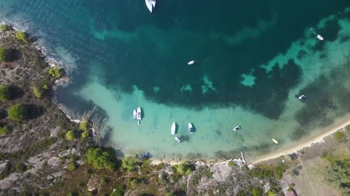 Overhead drone clip of a small tropical island bay with crystal blue water and luxurious boats in th