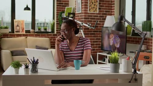 Woman Works on Laptop, Talks on Phone at Desk