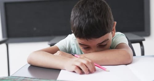 In a school classroom, a young boy rests his head on his arms