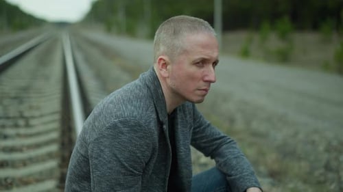 Man Sitting by Train Tracks in Rural Location