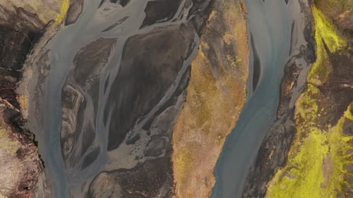 Flyover directly above Iceland riverbed of black volcanic sediment, dramatic landscape.