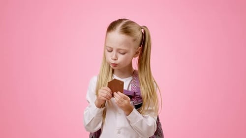 Child Shows Excitement While Eating Snack in a Studio With Pink Background