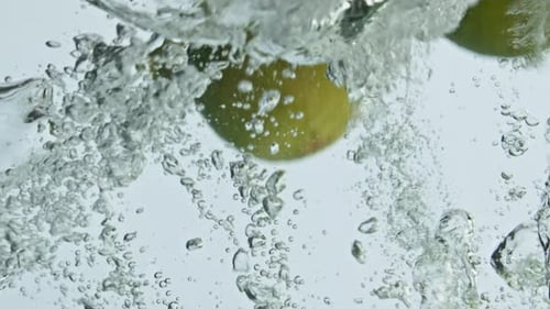 Limes Dropping Into Water Creating Bubbles and Splashes