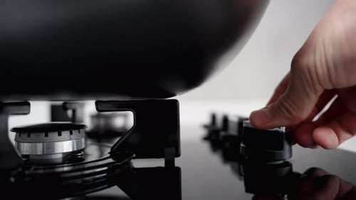 A close-up panoramic view shows the gas burner on the black stove being ignited with a large pot on