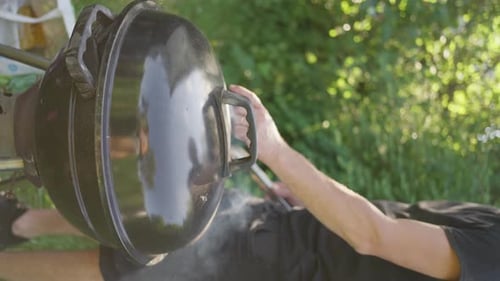 Man Cooking on Grill Closing Lid in a Round Grill in a Meadow Summer Picnic