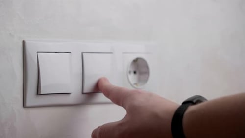 Imagem aproximada da mão de um homem desligando um interruptor de parede.