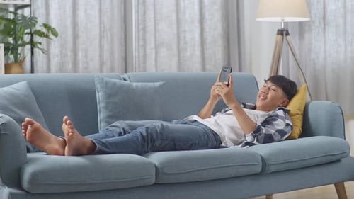 Young Adult Lying on Sofa Looking at Phone