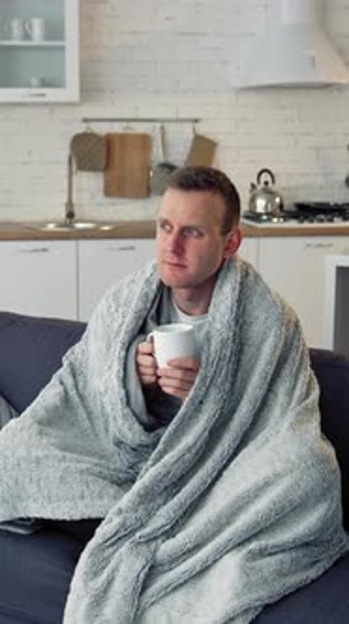Ill man drinking hot beverage at home.