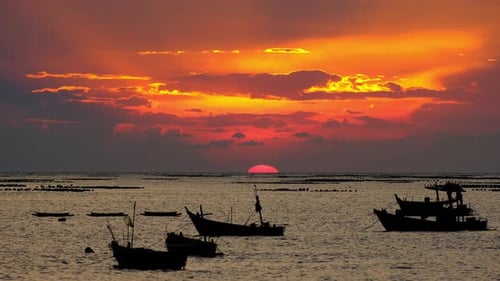 Dramatic sunset at the ocean with many boats on foreground.