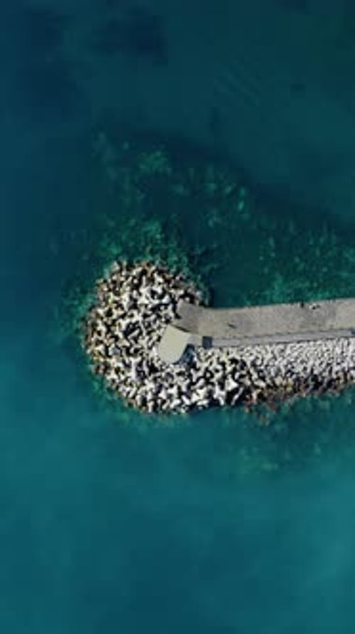 Vista aérea vertical de cima para baixo de um drone de pessoas caminhando na extensão do cais de quebra-mar de pedra curva