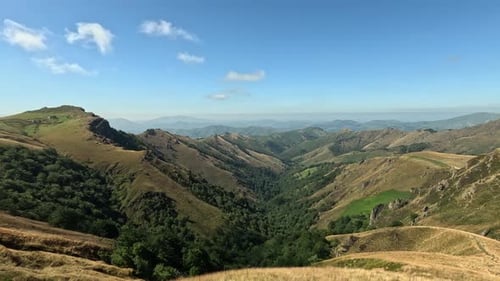 Paisagem de cordilheira verde acidentada se estende até um distante horizonte ensolarado