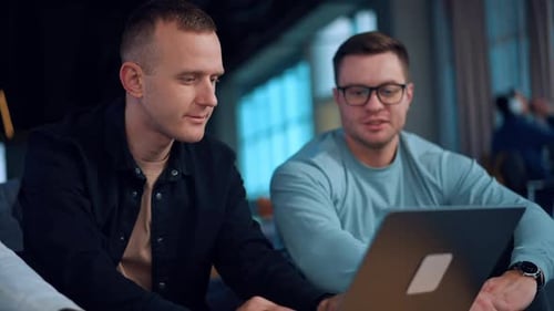Two young men sitting indoors in front of laptop.