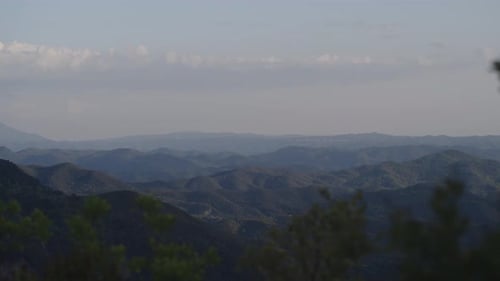 Ein ruhiger Fernblick auf geschichtete Bergkämme, die unter einem zartblauen Himmel in den Horizont übergehen.