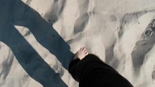 Bare feet of woman in black pants walking on sand