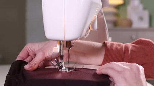 Woman sewing fabric with professional machine in workshop, closeup