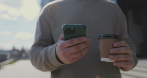 Close Up of a Man Drinking to Go Coffee and Browsing Smartphone Social Networking at Urban Modern