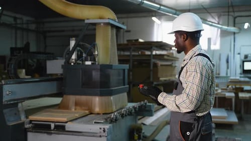 Afroamerikanischer Arbeiter steuert CNC-Holzschneidemaschine aus der Ferne