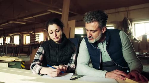 Man And Woman Workers In The Carpentry Workshop, Making Plans.