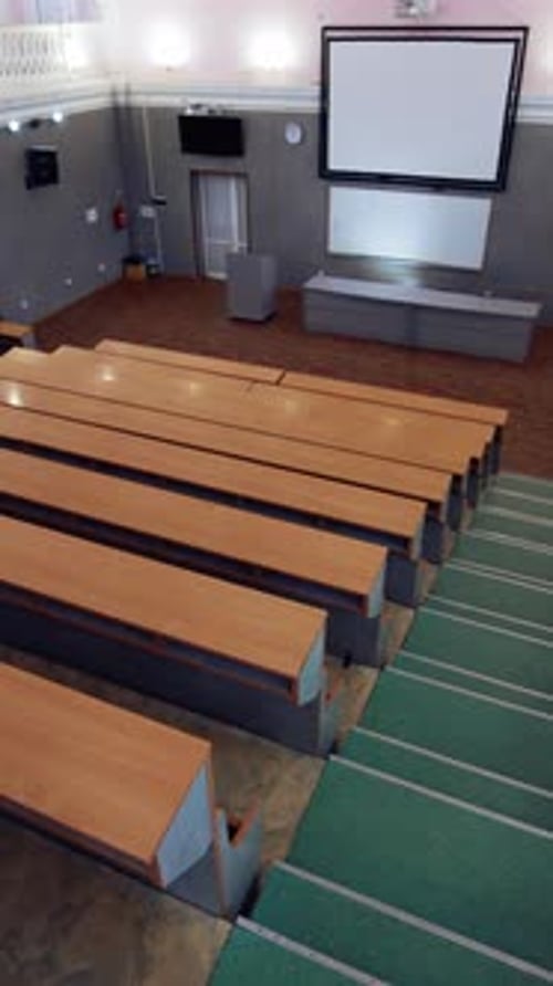 Modern hall for meetings. Large university auditorium with row of desks and a large white board.