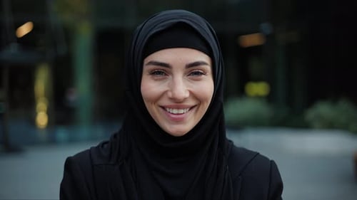 Erfolgreiche schöne muslimische Geschäftsfrau blickt in die Kamera und lächelt