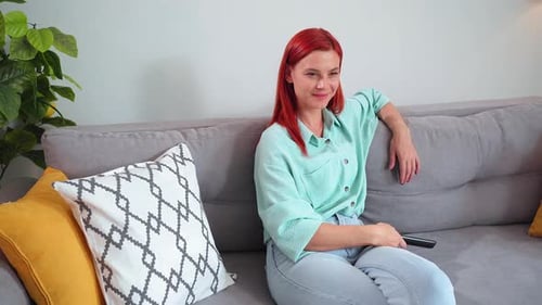 Woman Sits on Couch, Watching Television