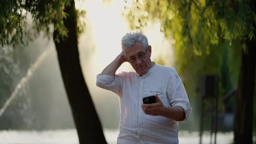 Pensive Senior Man with Smartphone Outdoors Elderly Man in Thoughtful Pose with Smartphone in Park
