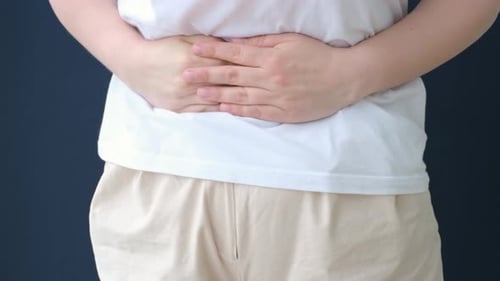 Woman holding her belly close-up on blue background, front view.