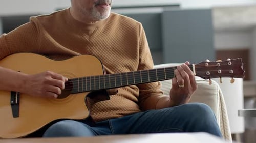 Man Plays Acoustic Guitar Sitting on Couch