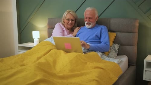 Senior Couple Enjoying Laptop in Bed Together