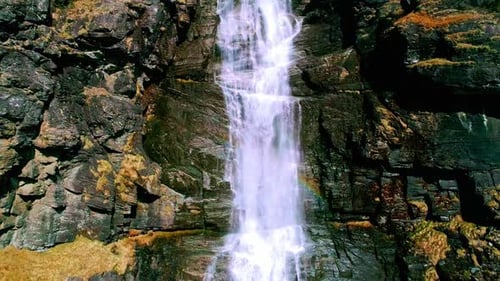 Descending drone footage of a beautiful waterfall flowing down the rocks.