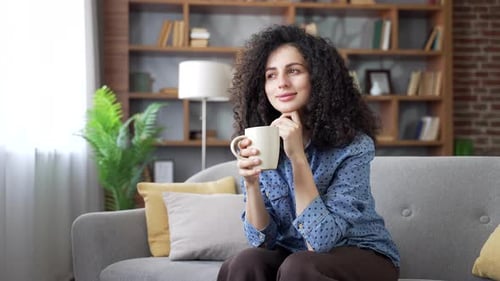 Thoughtful Woman Relaxing on Sofa with Coffee