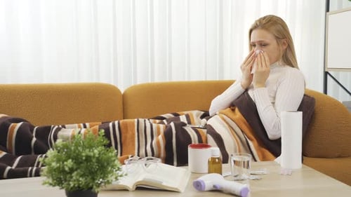 Woman Lying on Couch Blowing Nose with Tissue