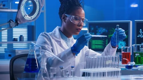 A Young African American Woman Using a Plastic Pipette Pipettes Red and Green Liquid Into Glass Test