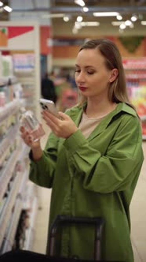 Woman Using Smartphone Scanning Product in Supermarket Aisle
