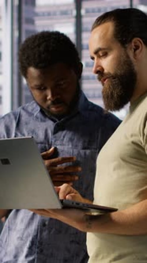 Vertikaler Videoentwickler und Kollege überprüfen Code auf dem Notebook beim Brainstorming