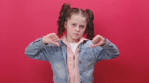 Portrait of serious preteen girl kid showing thumbs down sign gesture, expressing discontent
