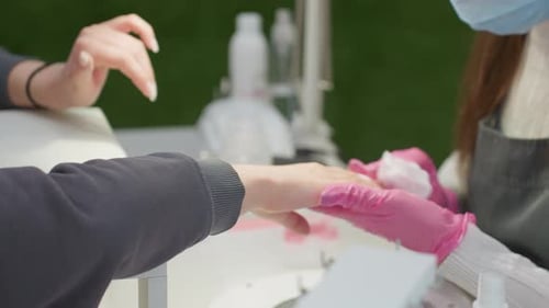 Nail Technician Cleaning Client Hand Beside Green Wall Under Bright Light