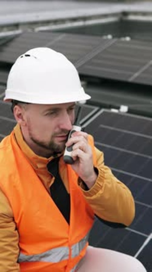 Ein Ingenieur mit einem Walkie-Talkie inspiziert Sonnenkollektoren auf dem Dach eines Hauses.