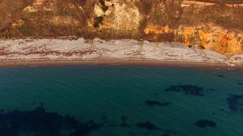 Flying over sea-green water at the rocky coast. View on the narrow sandy