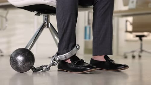 Businessman with metal ball and chain on his leg in office, closeup