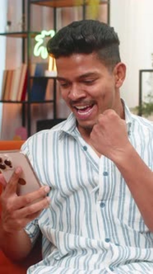 Excited young man looking at mobile phone indoors