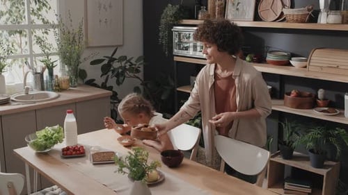 Woman Serves Breakfast to Child at Kitchen Table