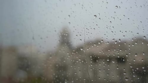 A slow-motion of raindrops seen through a window during heavy rainfall, with an urban city landscape