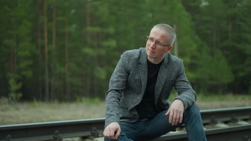 Pensive Man Sitting on Railway Tracks in Forest