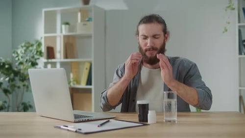 Man Taking Medicine for Headache at Desk