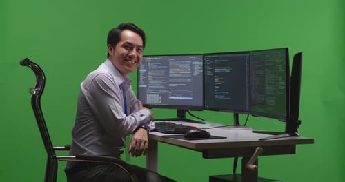 Developer Smiling To Camera While Write Code With Multiple Computer Screens In Green Screen Studio
