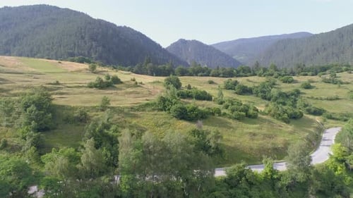 AERIAL: flying over arable land in a mountainous area, mountains can be seen in the background.